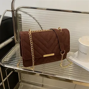 Close-up of deep brown suede shoulder bag with V-shaped quilting and gold metal chain strap