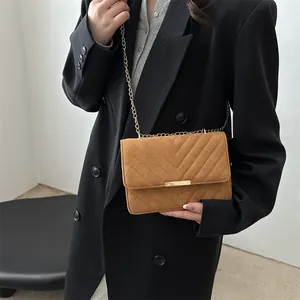 Vintage brown suede chain bag with V-shaped quilting and gold metal lock on black blazer