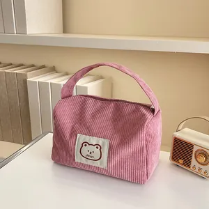 Detailed close-up of pink corduroy makeup bag with cute bear patch on a clean white desk