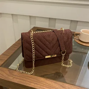 Deep brown chevron stitched crossbody bag with gold chain strap on a glass table