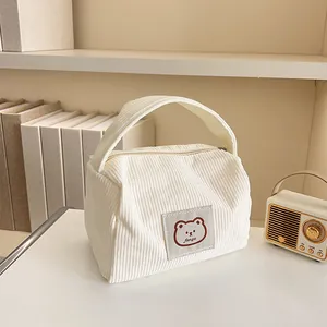 Detailed close-up of white corduroy cosmetic bag with bear patch and sturdy handle