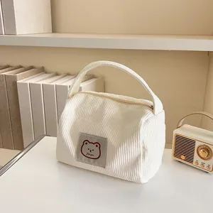 Close-up of cream corduroy cosmetic bag featuring a cute bear tag and soft texture