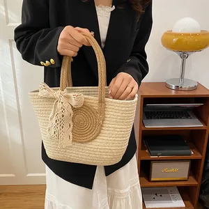 Close-up of beige woven tote bag with lace bow and spiral detail held by a model
