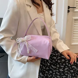 Detail of lavender mini handbag with pearl lace bow charm held by model in white blazer