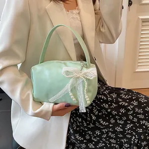 Detail of mint green satin handbag with large white lace bow and pearl tassel decor