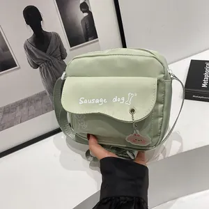 Close-up of light green canvas crossbody bag with sausage dog print and cute charm