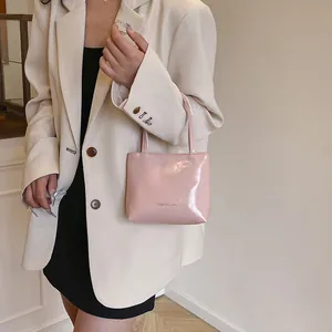 Dettaglio mini borsa rosa lucida con logo portata a mano da una modella chic