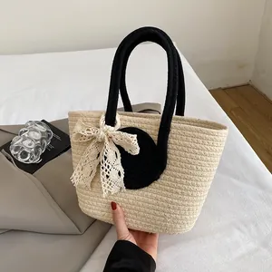 Detailed close-up of woven straw handbag featuring a lace bow and black top handles
