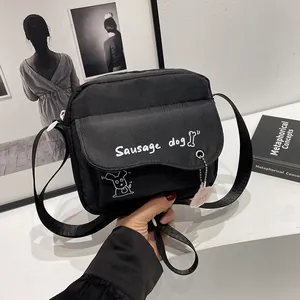 Detail of black canvas crossbody bag featuring a cartoon sausage dog print and doll pendant