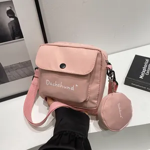 Pink canvas crossbody bag detail showing letter print and small round coin purse charm