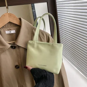 Dettaglio di una mini borsa verde chiaro in pelle con doppi manici e logo argento
