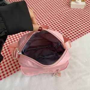 Pink nylon crossbody bag with wide strap, peach pendant and interior zipper pocket
