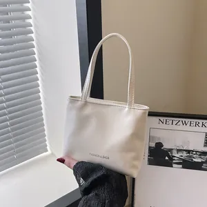 Dettaglio della borsa a mano minimalista in pelle crema con sottili manici e scritte