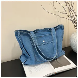 Detailaufnahme der blauen Denim-Tragetasche mit vorderer Druckknopftasche und weicher Textur