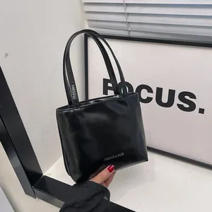 Dettaglio mini borsa nera in pelle verniciata lucida con manici sottili e scritte argento