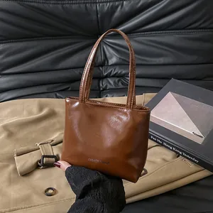 Dettaglio di una borsa a mano in pelle marrone lucida con manici lunghi e logo testo