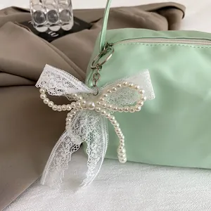 Detail of light green handheld bag featuring a pearl bow and lace zipper pendant