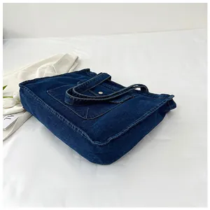 Detail der dunkelblauen Denim-Tragetasche mit weißen Kontrastnähten und Metalldruckknopf