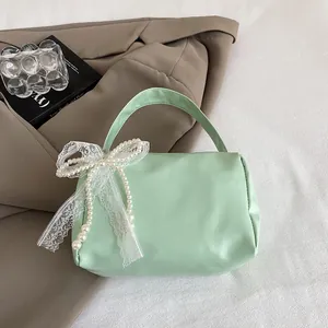 Detail of mint green handbag featuring delicate white lace trim and pearl bow accent