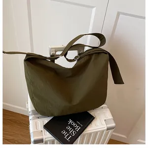 Detail of army green nylon crossbody bag with wide adjustable strap on white suitcase