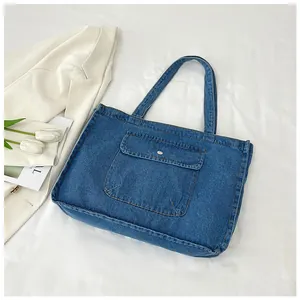 Dunkelblaue Denim-Tragetasche mit großer Fronttasche und Metallschnalle auf weißem Stoff
