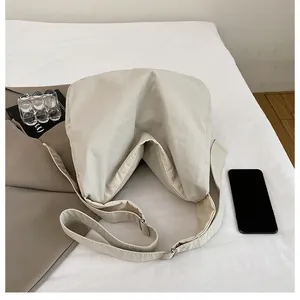 Flat lay of cream crossbody tote bag with adjustable wide strap on white sheets