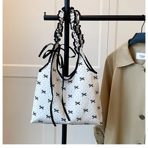Detail of white canvas shoulder bag with black bow prints and ruffled strap accents