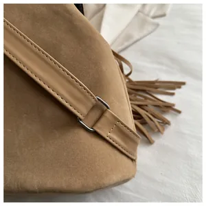 Detail of brown suede backpack showing long tassel accents and metallic ring buckle