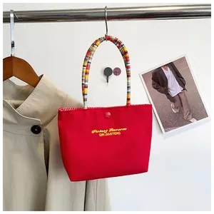 Detail of red nylon tote bag with yellow embroidery and colorful woven bead handle