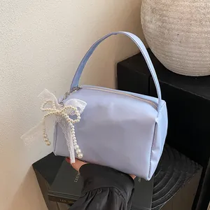 Detailed close-up of light blue satin handbag with delicate lace bow and pearl charms