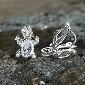 Macro shot of silver turtle clip-on earrings with sparkling zircon stones on a grey rock