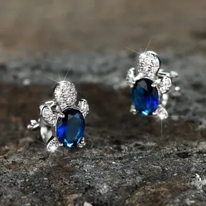 Macro shot of silver turtle earrings with blue gems on a grey stone surface