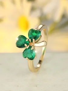 Close-up of golden clover ring featuring three heart-cut emerald gemstones with sparkles