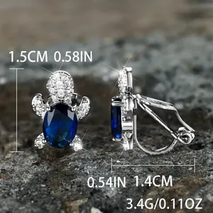 Turtle stud earrings with blue zircon and white crystals on a dark stone background