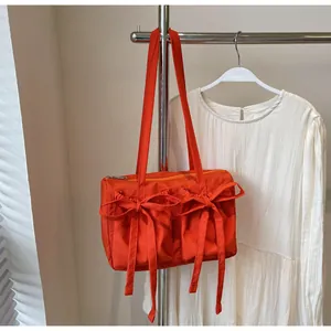 Détail du sac cabas orange vif avec poches décoratives à nœuds et fermeture éclair en métal