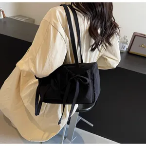 Détail du sac cabas en nylon noir avec grand nœud décoratif et bandoulière minimaliste