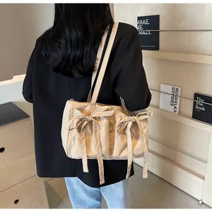 Détail d'un sac cabas beige avec nœuds porté à l'épaule montrant le tissu souple