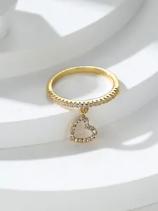 Dettaglio di un anello dorato con ciondolo a cuore e cristalli lucidi su base bianca