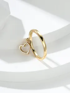 Primo piano di un anello dorato con pendente a cuore pavé su un palco bianco minimalista