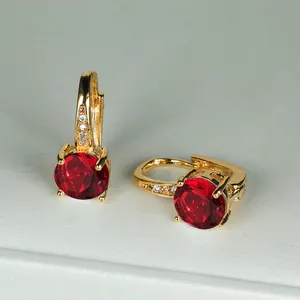 Dettaglio di orecchini a cerchio dorati con grande zircone rosso tondo a quattro griffe