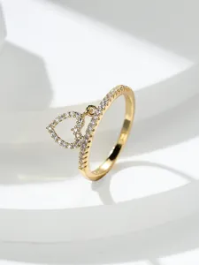 Dettaglio anello dorato con ciondolo a cuore e zirconi su supporto geometrico bianco
