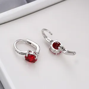 Vista macro di orecchini huggie in argento con zircone rosso e piccoli cristalli