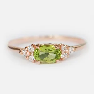 Dettaglio di un anello in oro rosa con gemma verde ovale e accenti di zircone bianco