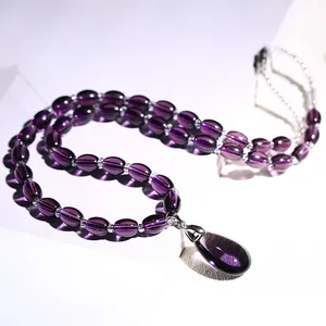 Collar de cuentas violetas con un colgante de cristal en forma de gota sobre blanco