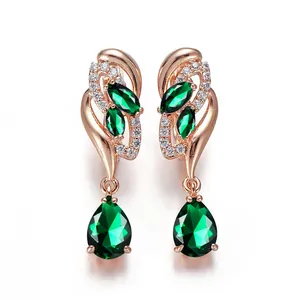Close-up of rose gold earrings with teardrop emerald stones and white diamond accents