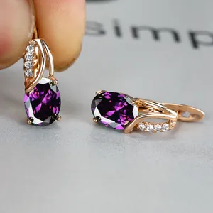Macro view of rose gold huggie earrings with oval purple zircon and white crystal accents