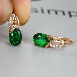 Macro detail of rose gold earrings with emerald green oval zircon stones and pavé accents