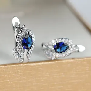 Detail van zilveren huggie oorbellen met blauwe druppelstenen en pavé kristallen
