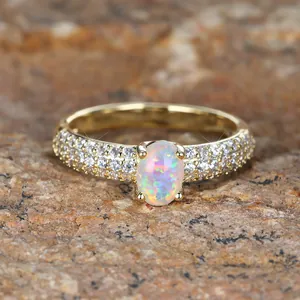 Golden oval opal ring with pavé diamond band set on a textured natural stone background