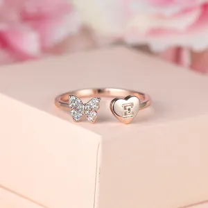 Détail de la bague papillon or rose avec cœur lettre E sur un support de présentation